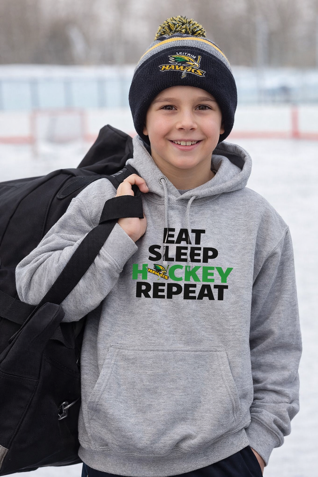 Child wearing a gray hoodie with 'Eat Sleep Hockey Repeat' text, holding a hockey bag on a snowy background.