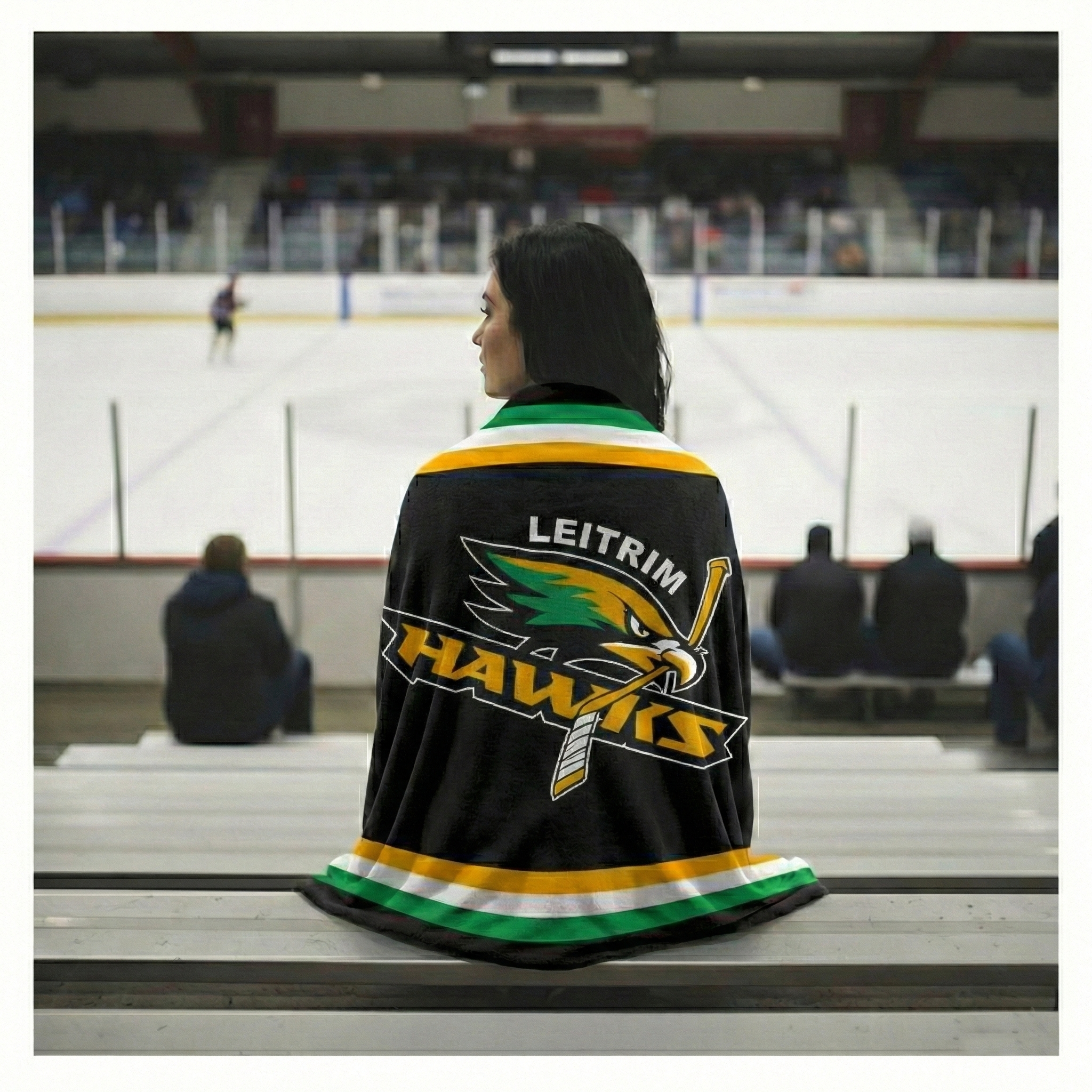 Person wearing a Leitrim Hawks sports team blanket at an ice hockey game.